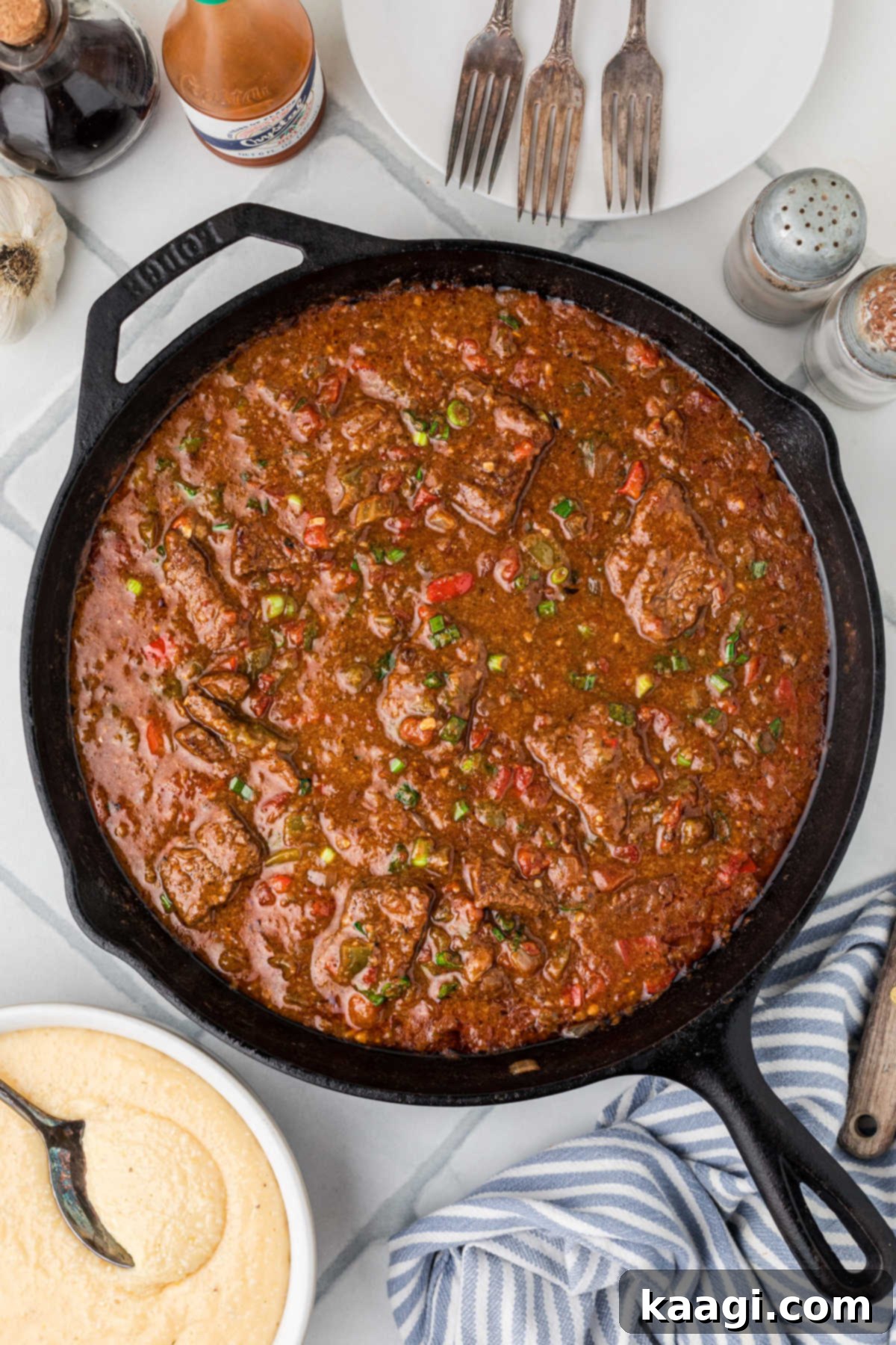 Overhead shot of a pan full of grillades, with a bowl of cheesy grits on the side for serving.