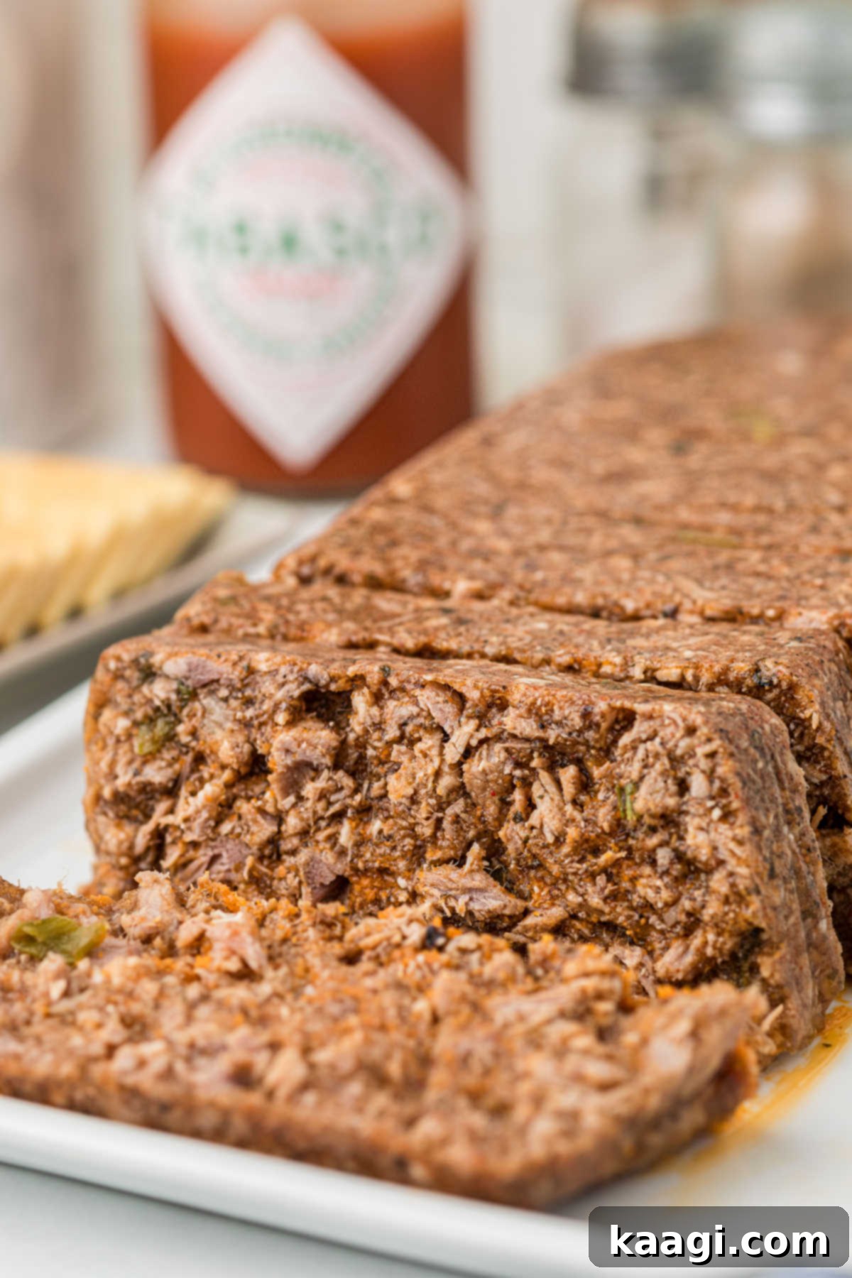 A close-up view of a whole loaf of mock hog head cheese, with several perfectly cut slices revealing its meaty texture and vibrant seasoning.
