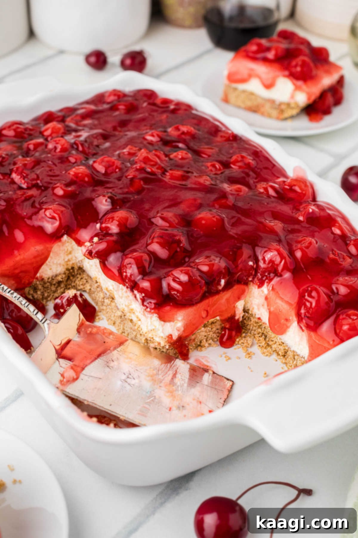 A dish of Old Fashioned Cherry Delight with some servings already taken, revealing the layers of crust, cream cheese, and cherry topping.