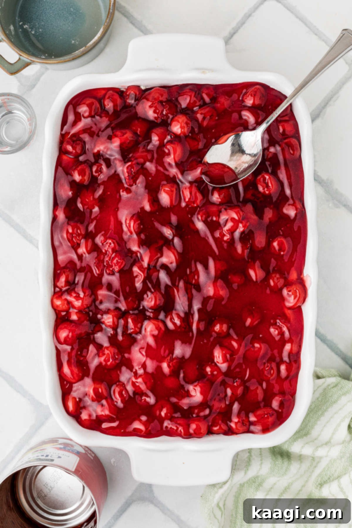 Cherry Pie filling being smoothly spread on top of the cream cheese layer in the baking dish.