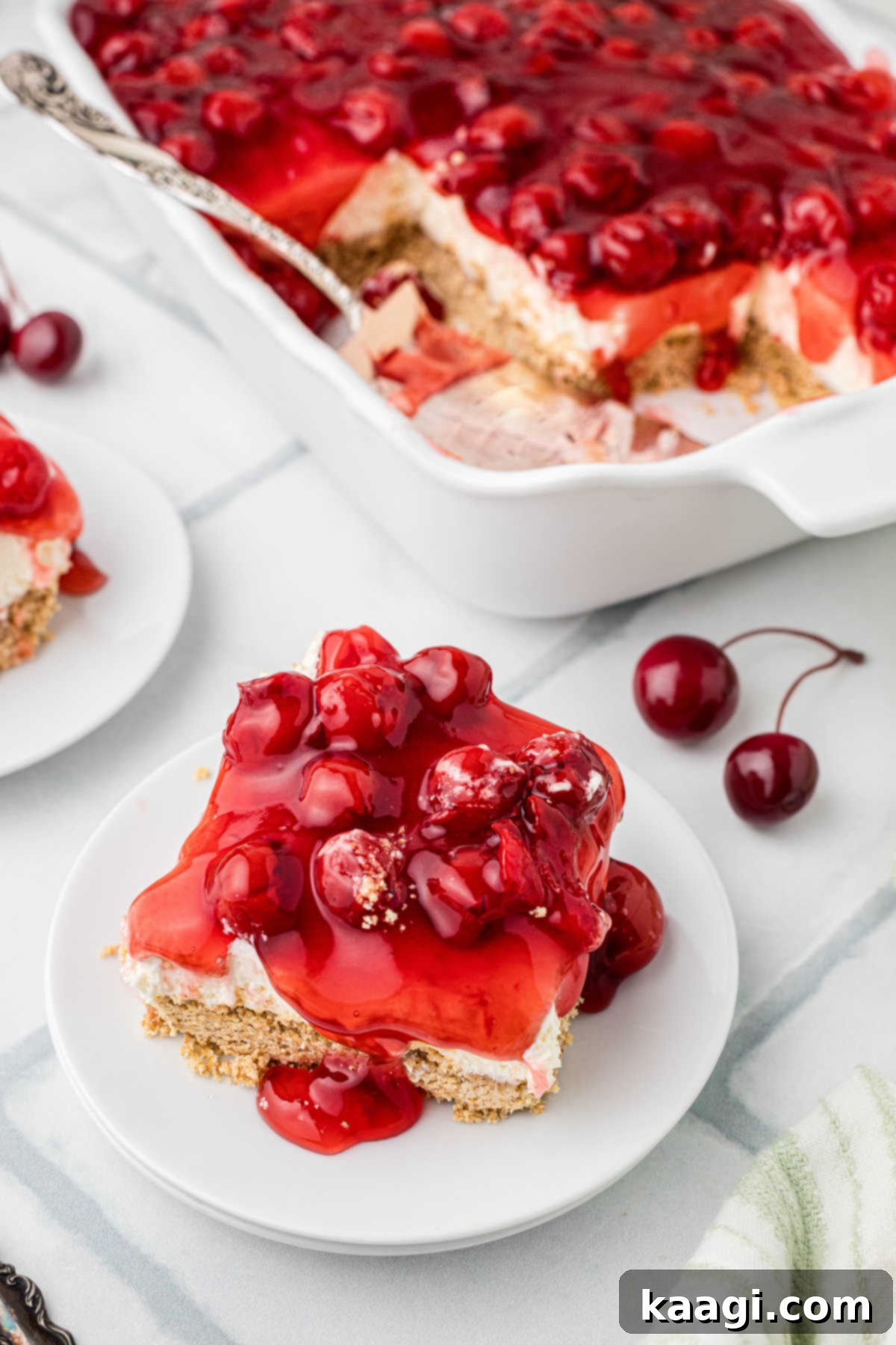 A close-up shot of a single slice of Old Fashioned Cherry Delight on a plate, positioned in front of the larger dish.