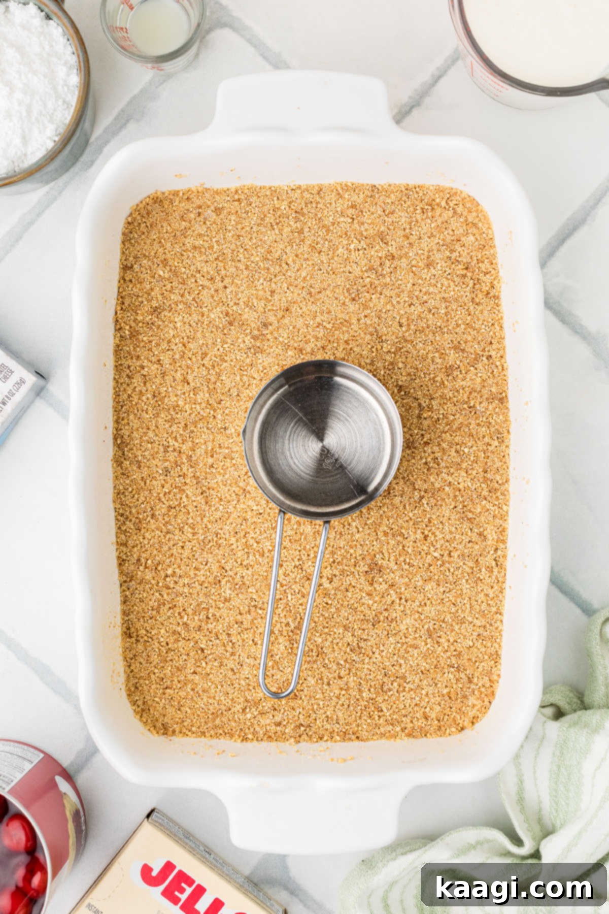 The graham cracker crumb mixture being pressed firmly into the bottom of a 13x9 inch baking dish.