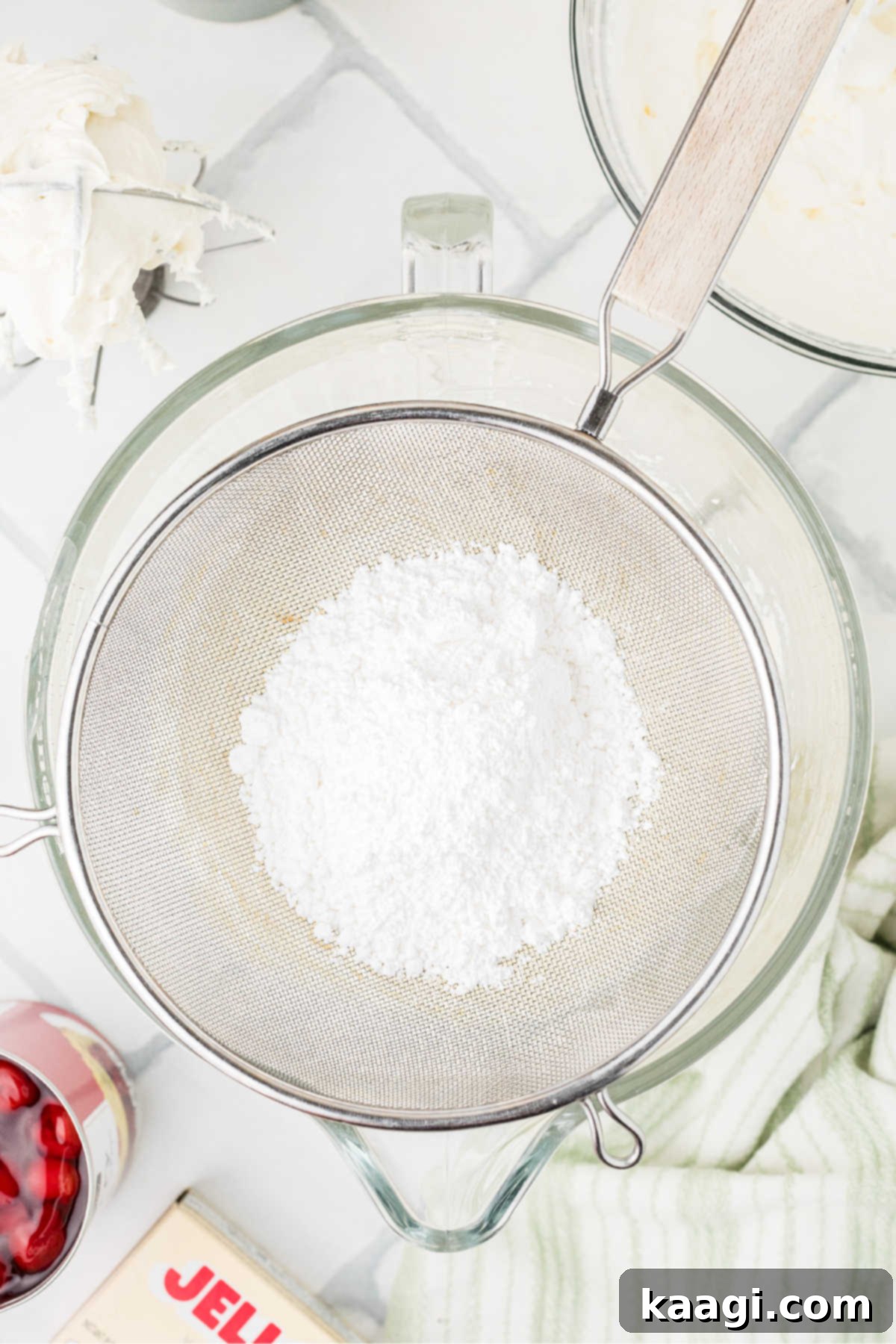 Powdered sugar being passed through a sieve into the cream cheese mixture to prevent lumps.