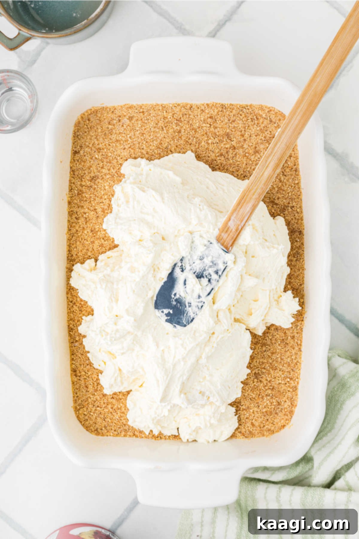 The creamy cream cheese filling being spooned evenly on top of the graham cracker crust base.