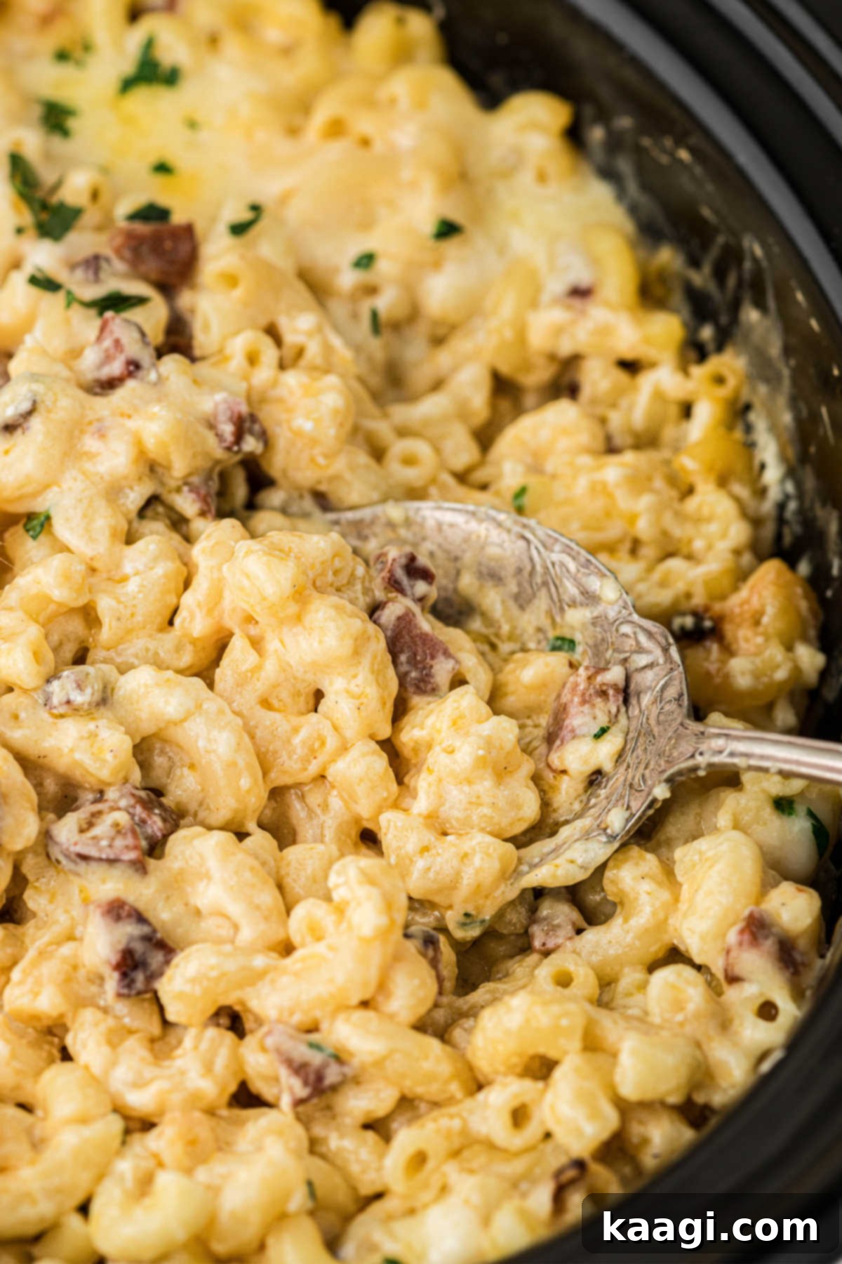 Close up of a spoon resting in a slow cooker that has Cajun mac and cheese in it, showcasing the creamy texture and rich color.