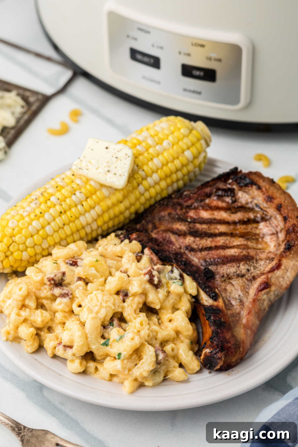 A plate with a grilled pork chop, corn on the cob and a generous pile of slow cooker Cajun mac and cheese, showcasing a complete meal.