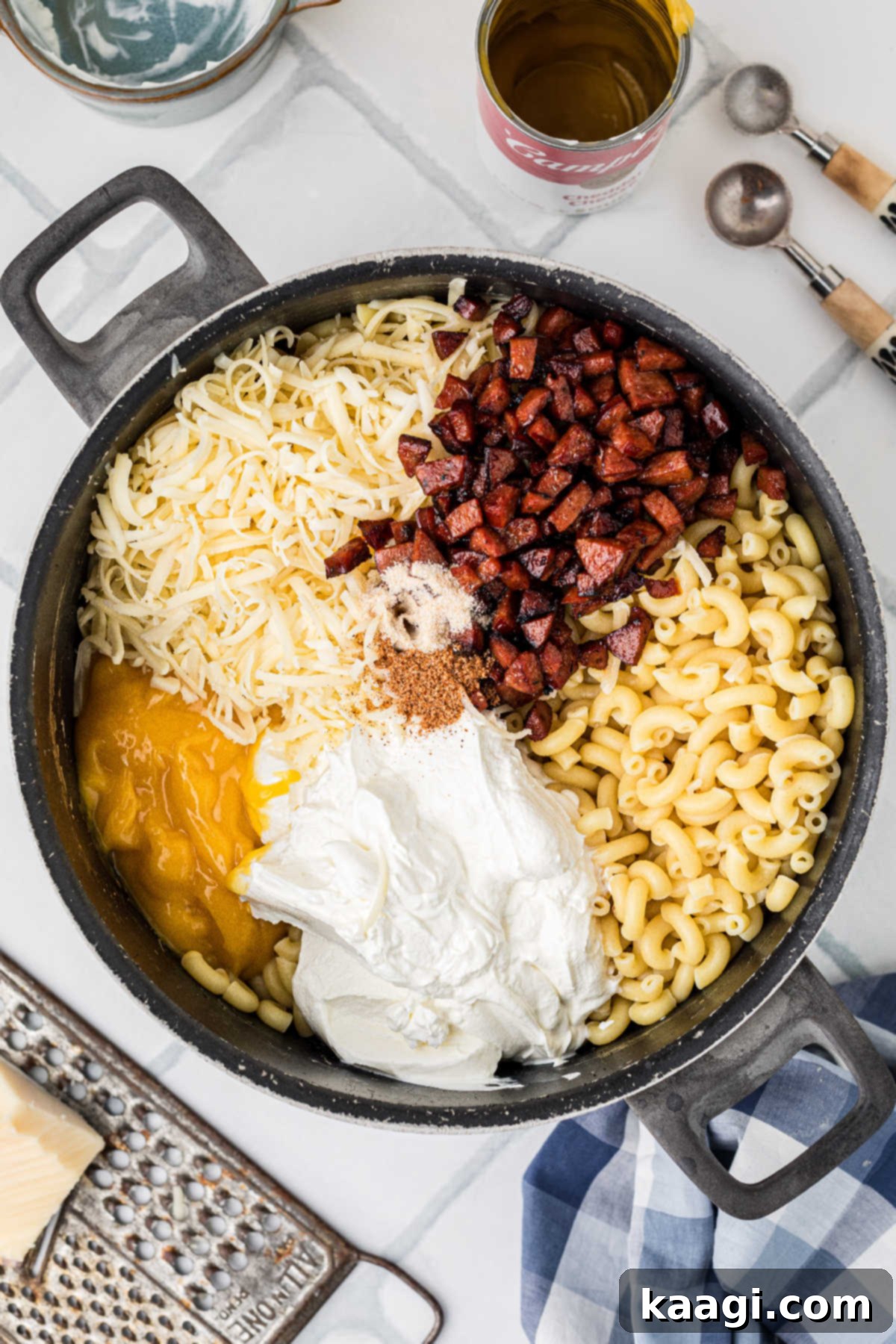 That same pot, now filled with cooked macaroni, caramelized sausage, sour cream, and grated cheeses, being stirred together.