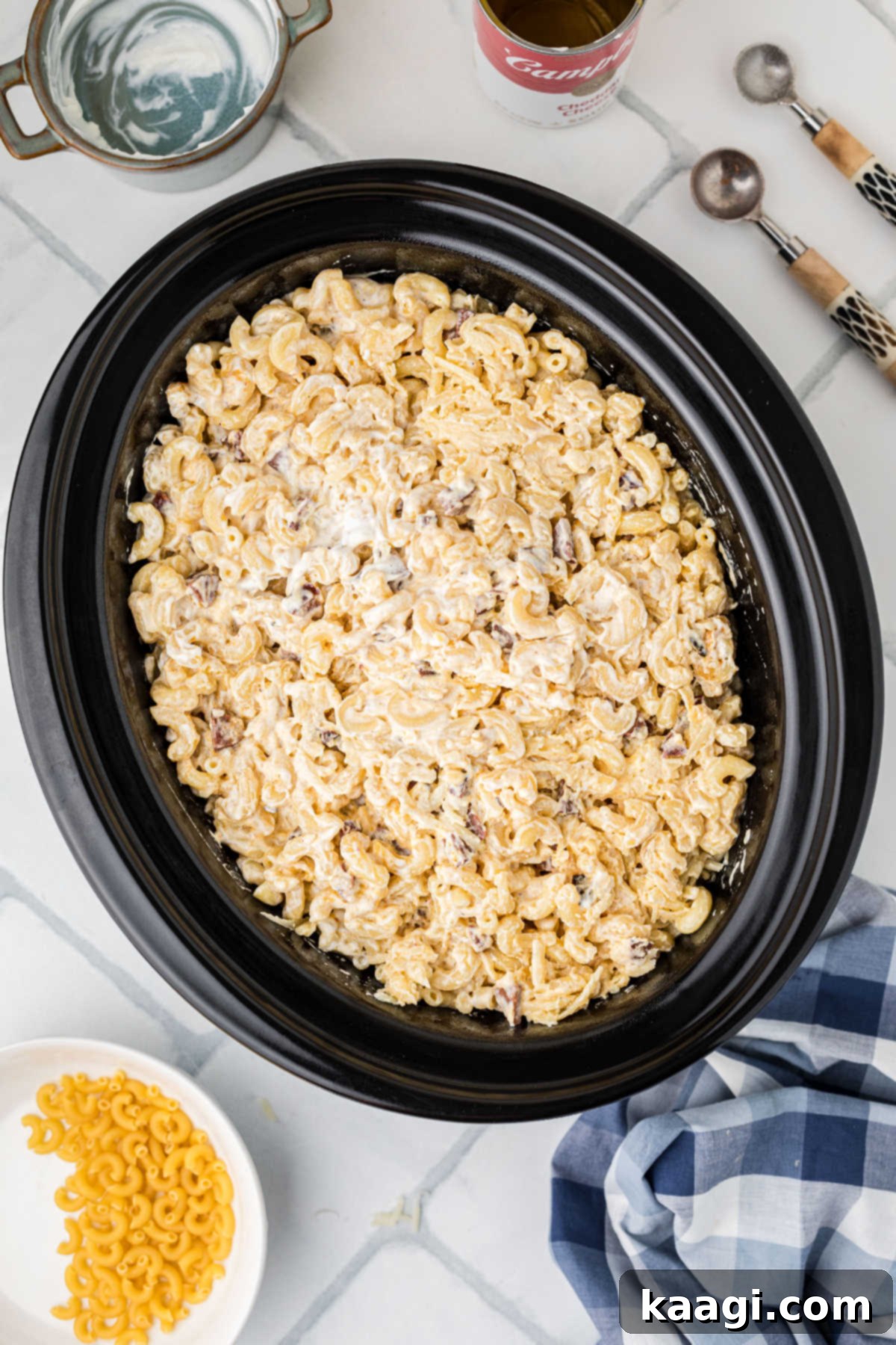 The combined Cajun mac and cheese mixture being transferred into a large, greased crock pot.