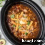 An overhead shot of a black crock pot with some chicken tortilla soup ready to be eaten.