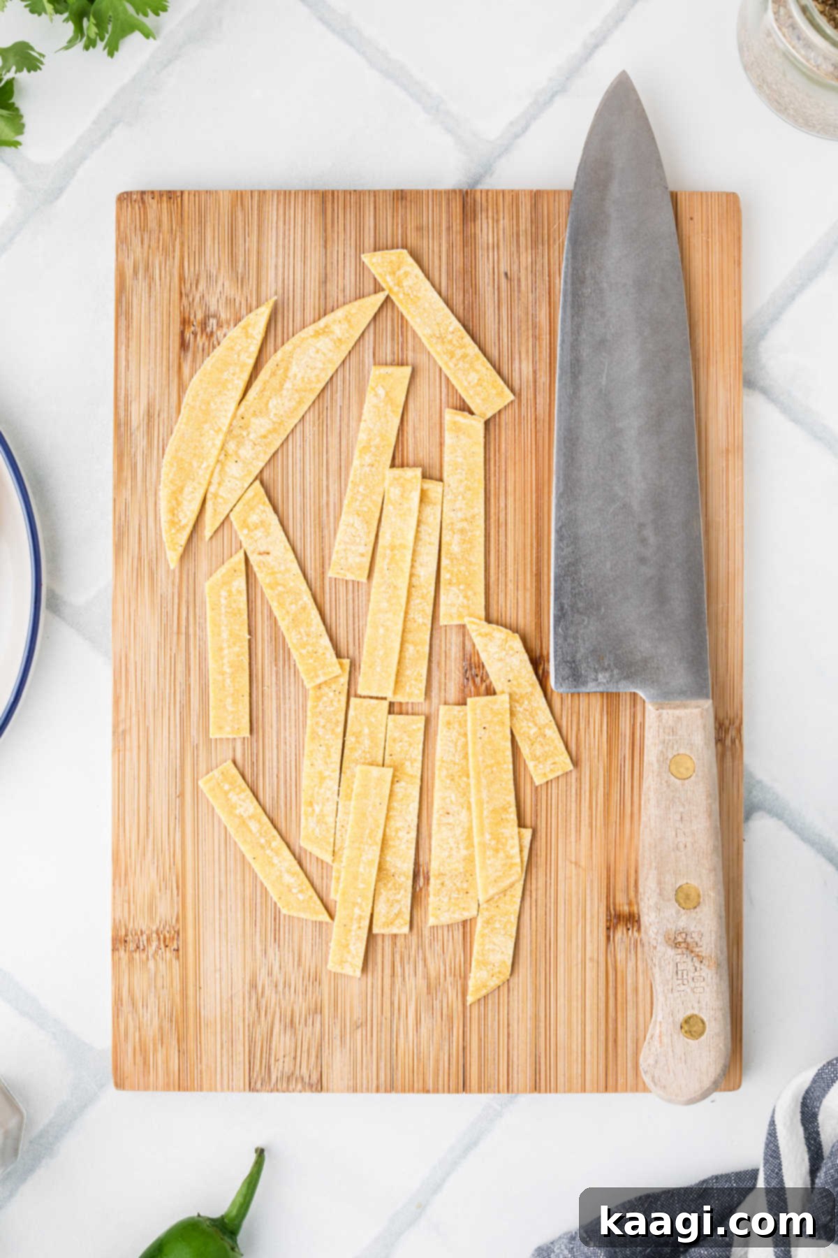 A wooden chopping board with a sharp knife next to a pile of freshly sliced corn tortilla strips, ready for frying.