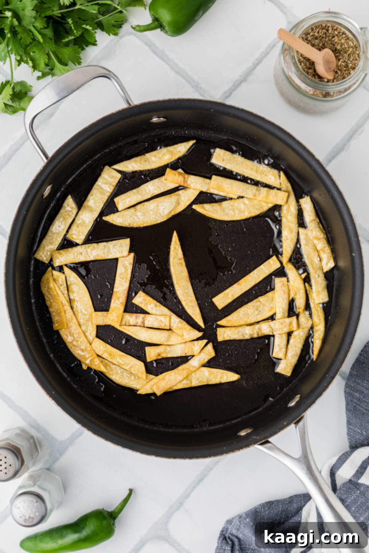 A frying pan on a stovetop, frying corn tortilla strips until golden and crispy.