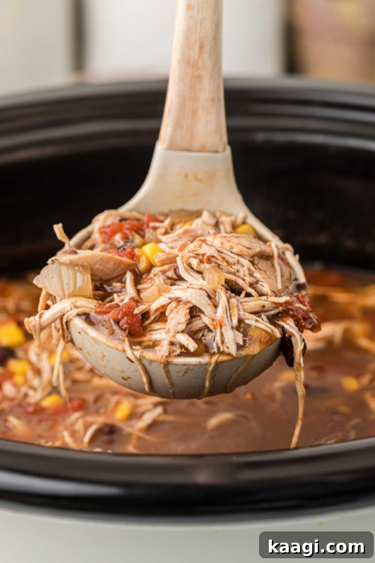 A ladle filled with the rich, vibrant slow cooker chicken tortilla soup, ready to be poured into a bowl.