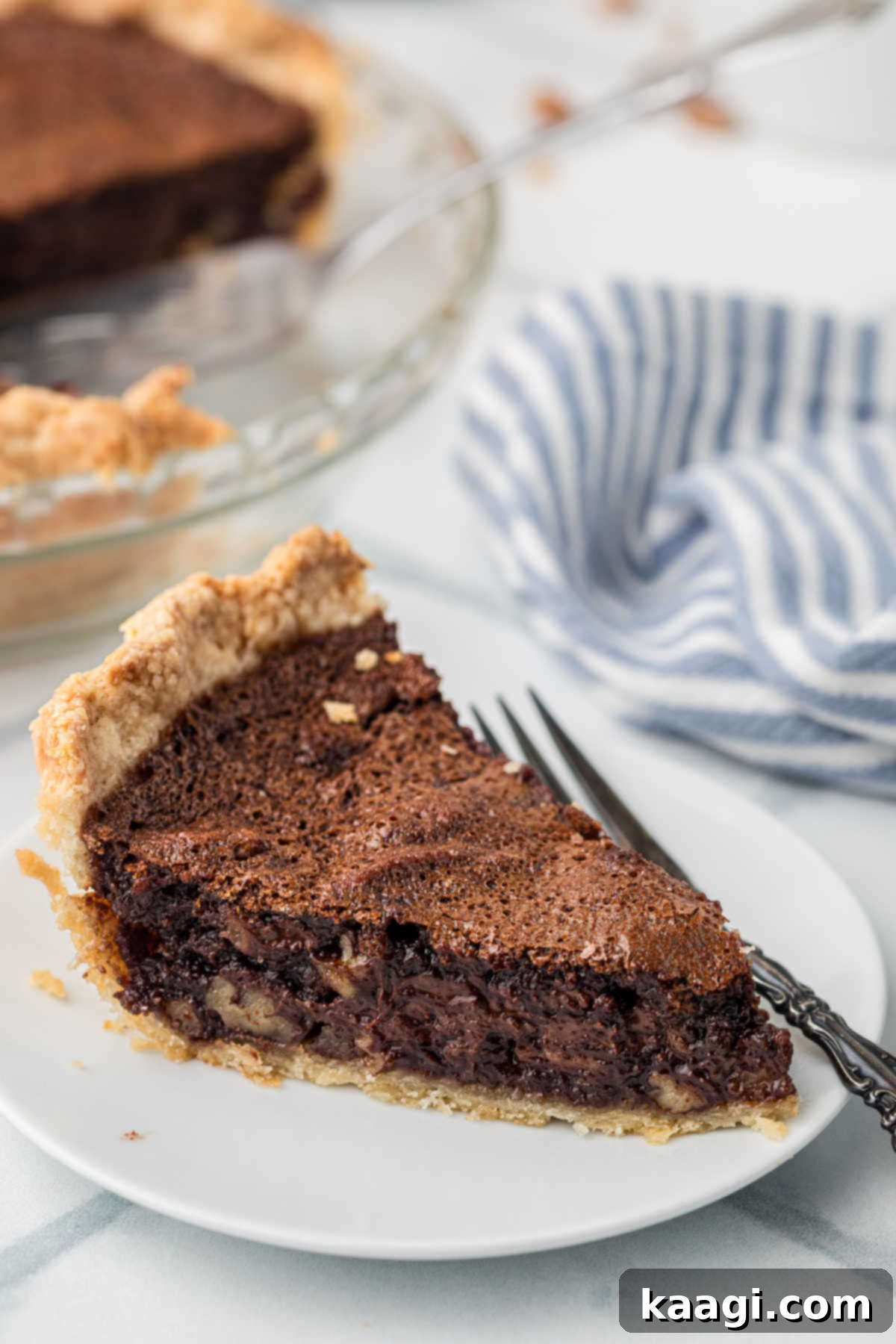 A perfectly portioned slice of chocolate pecan pie, featuring its rich, glossy filling and crunchy pecan topping, served elegantly on a white plate, ready to be enjoyed.