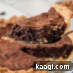 A slice of chocolate pecan pie with a rich, dark filling and crunchy pecans, being lifted from the pie dish, ready for serving.