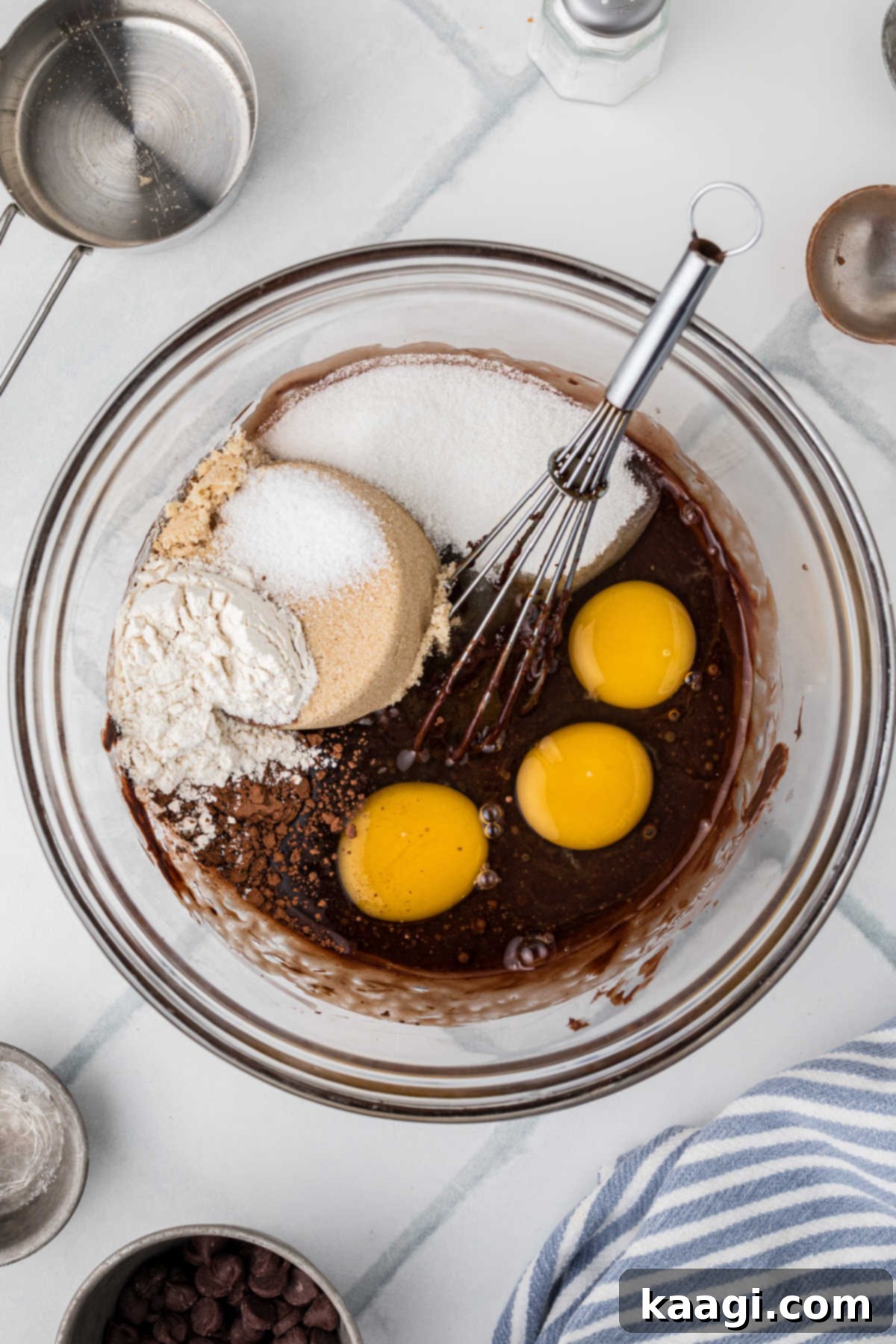 Various pie ingredients including eggs, sugars, and flour are carefully added to a bowl containing freshly melted chocolate and butter, ready to be combined into a rich filling.