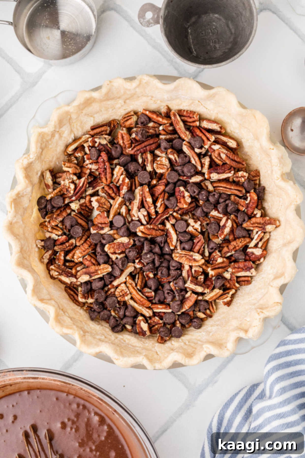 A prepared pie crust, carefully fluted around the edges, is generously filled with a layer of chopped pecans and a scattering of chocolate chips, forming the base of the pie.