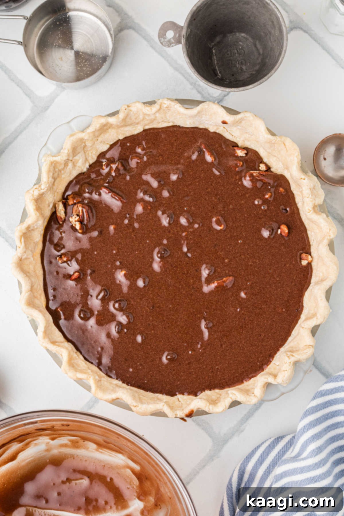 An unbaked chocolate pecan pie, with its rich filling poured over pecans and chocolate chips in a flaky crust, poised to be placed into a pre-heated oven for baking.