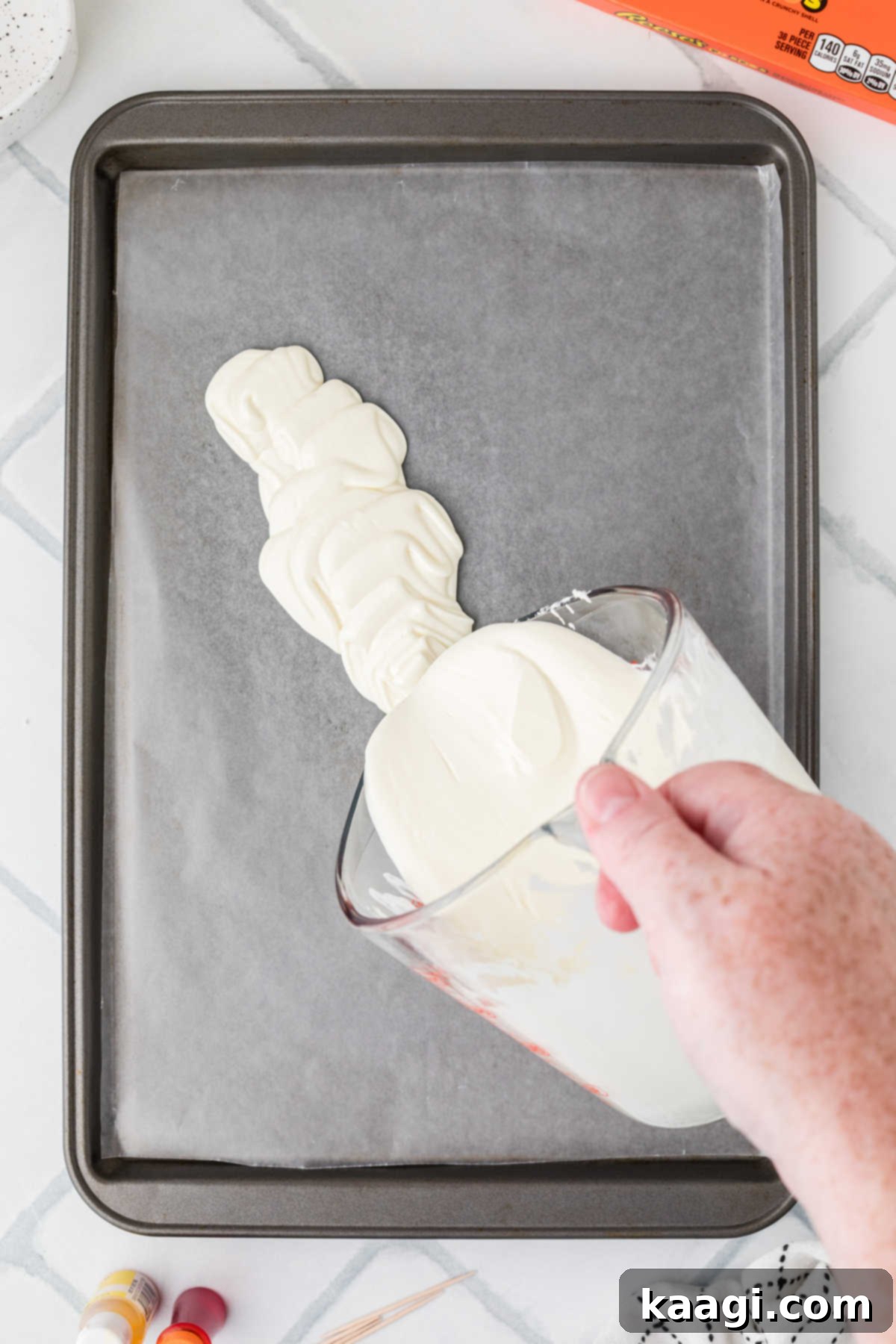 Creepy Crunch Bark 5 Melted white chocolate being poured onto a baking sheet lined with wax paper, forming a smooth base for the Halloween bark.