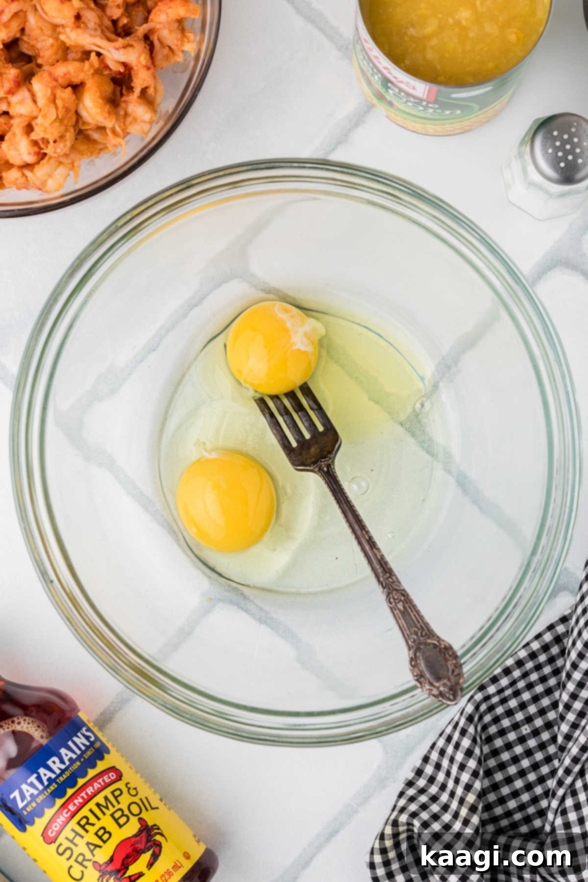 Cajun Crawfish Cornbread Muffins 4 Two fresh eggs cracked directly into a large glass mixing bowl, with a metal fork poised above them, ready to begin whisking to combine the yolks and whites.
