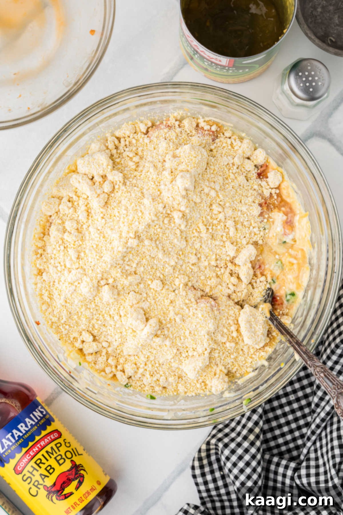Cajun Crawfish Cornbread Muffins 7 The fine contents of two boxes of Jiffy cornbread mix are being poured directly into the large mixing bowl, already containing the combined wet ingredients, crawfish, cheese, and vegetables.