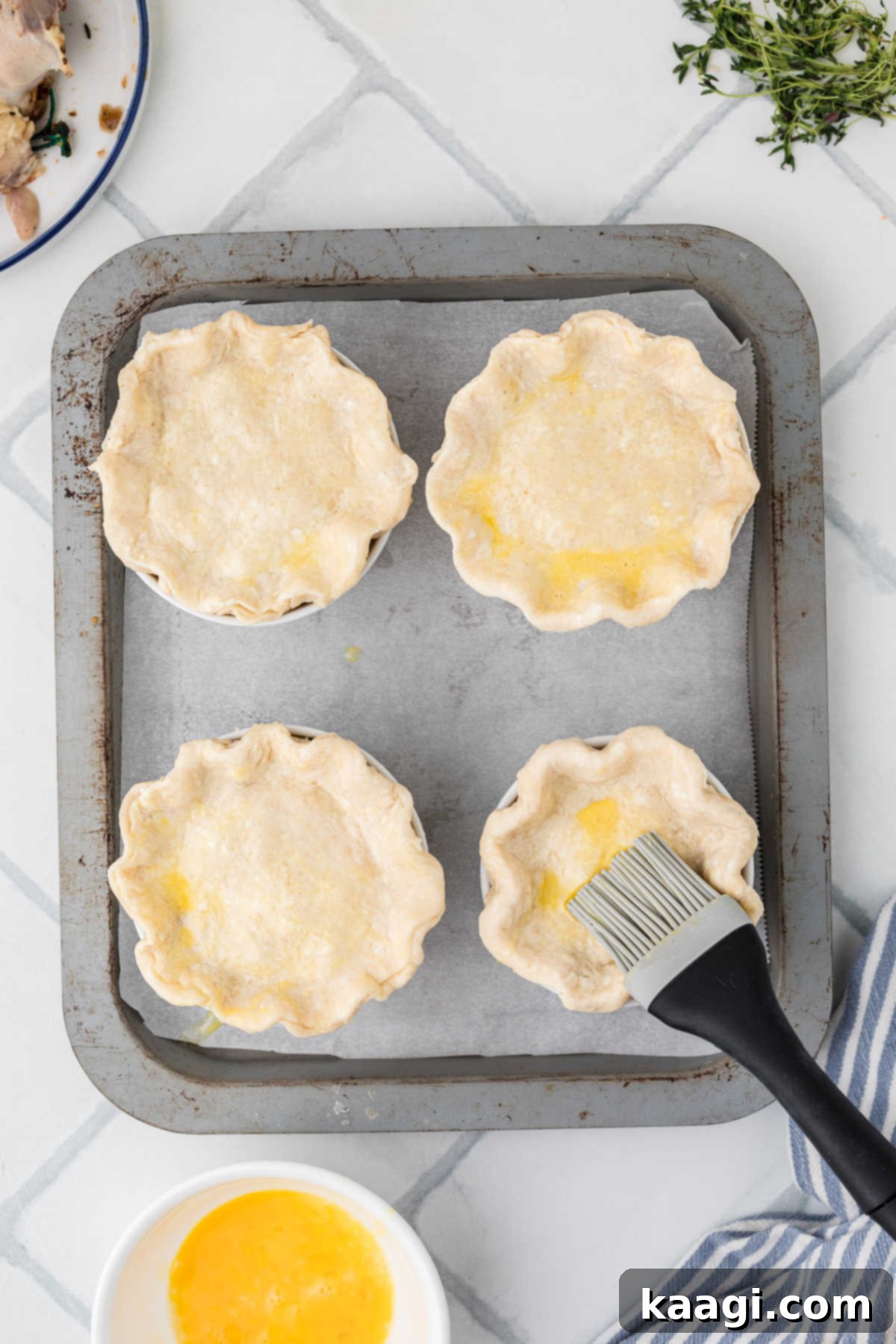 Comforting Mini Chicken Pot Pies 16 Mini chicken pot pies being brushed with a beaten egg for a golden finish.