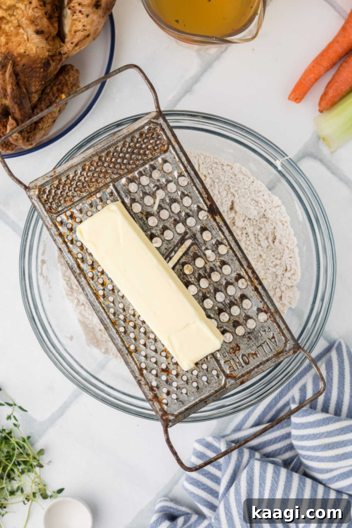 Comforting Mini Chicken Pot Pies 5 A grater with a stick of frozen butter, being grated into a bowl of flour mixture.