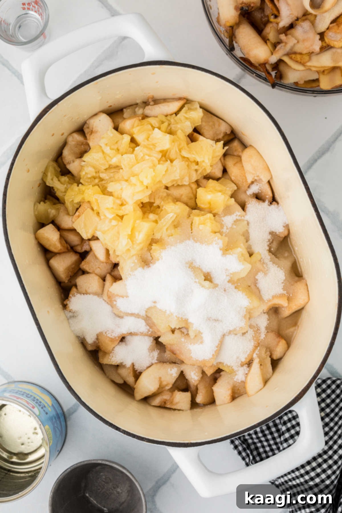A large heavy bottomed pot with some chopped pears, sugar, crushed pineapple and lemon juice, ready for cooking.