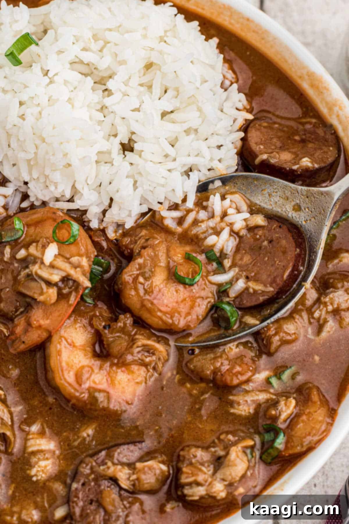 Close up shot of a Louisiana seafood gumbo recipe in a bowl with rice and a spoon digging in, showing the rich texture.