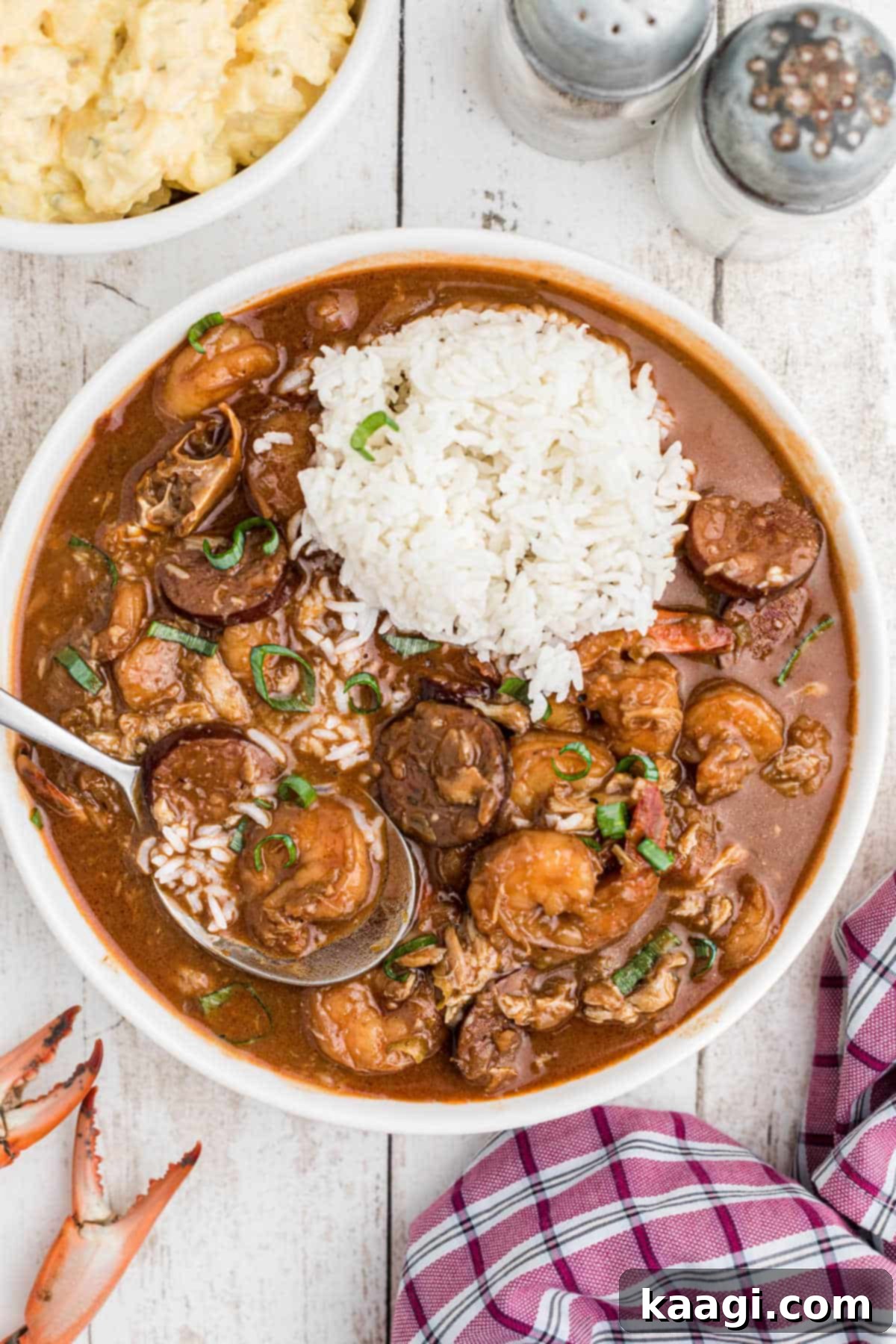 Overhead shot of a rich Louisiana seafood gumbo in a bowl, with a serving of white rice and a spoon digging in, emphasizing the abundant seafood.