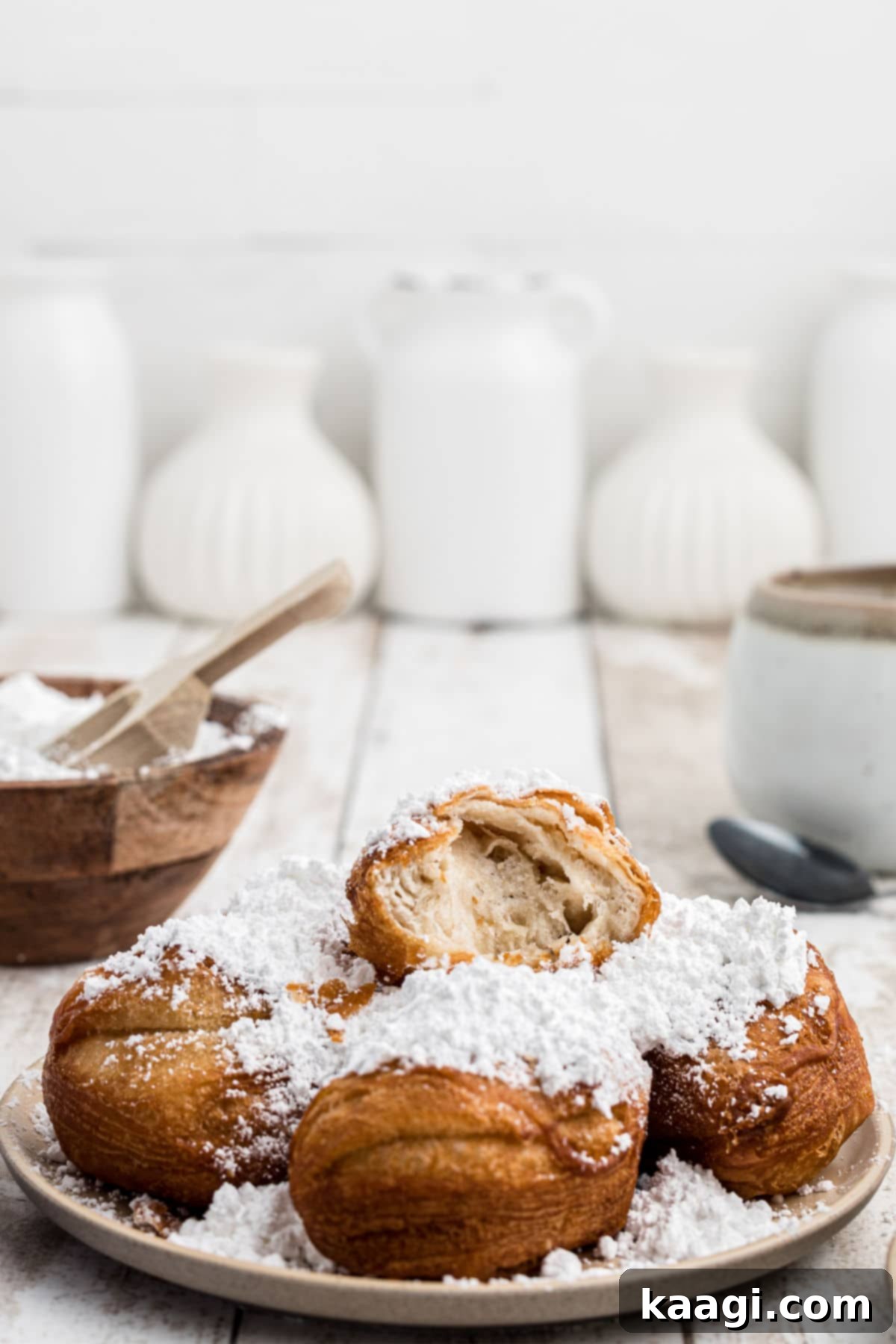 A plate of fluffy biscuit beignets, one with a bite taken out, revealing its soft interior, all covered in a snowdrift of powdered sugar.