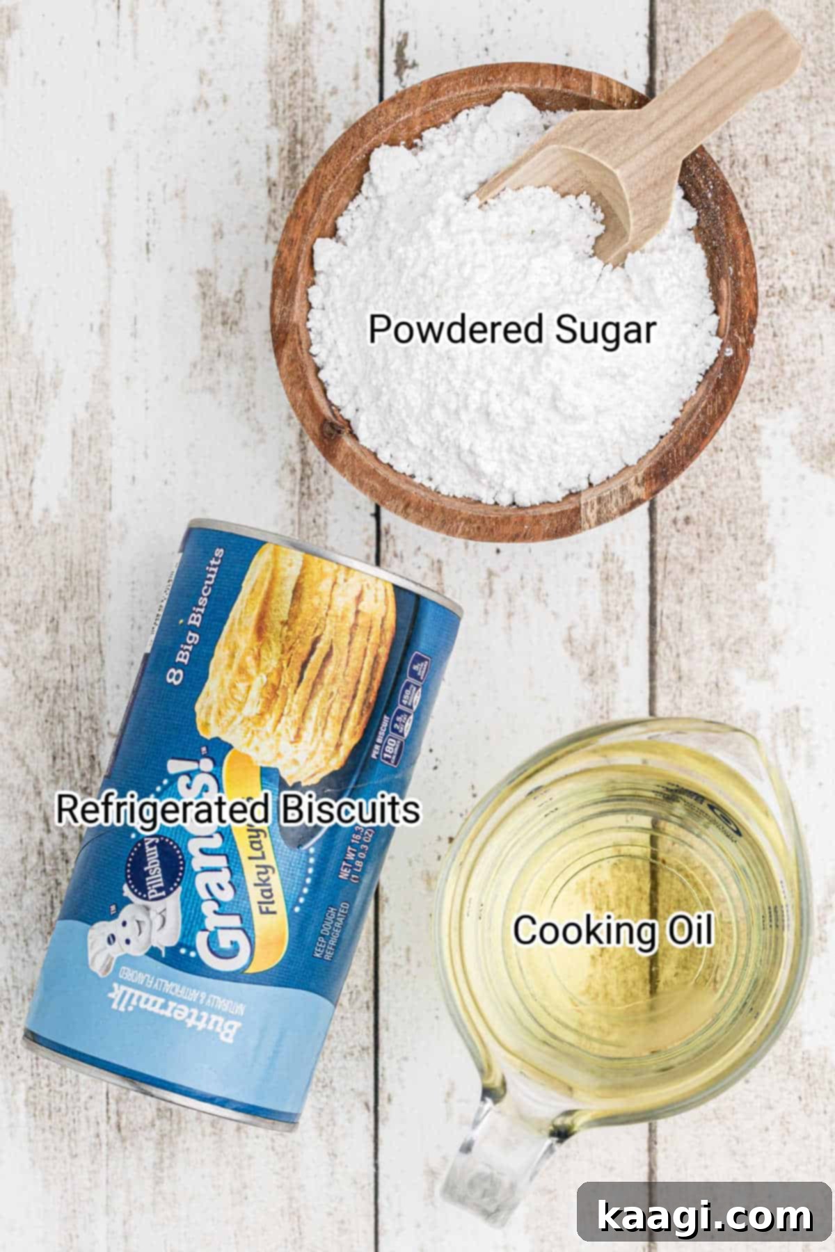 A simple flat lay of the three main ingredients for biscuit beignets: a can of refrigerated biscuits, a bowl of white powdered sugar, and a bottle of cooking oil.