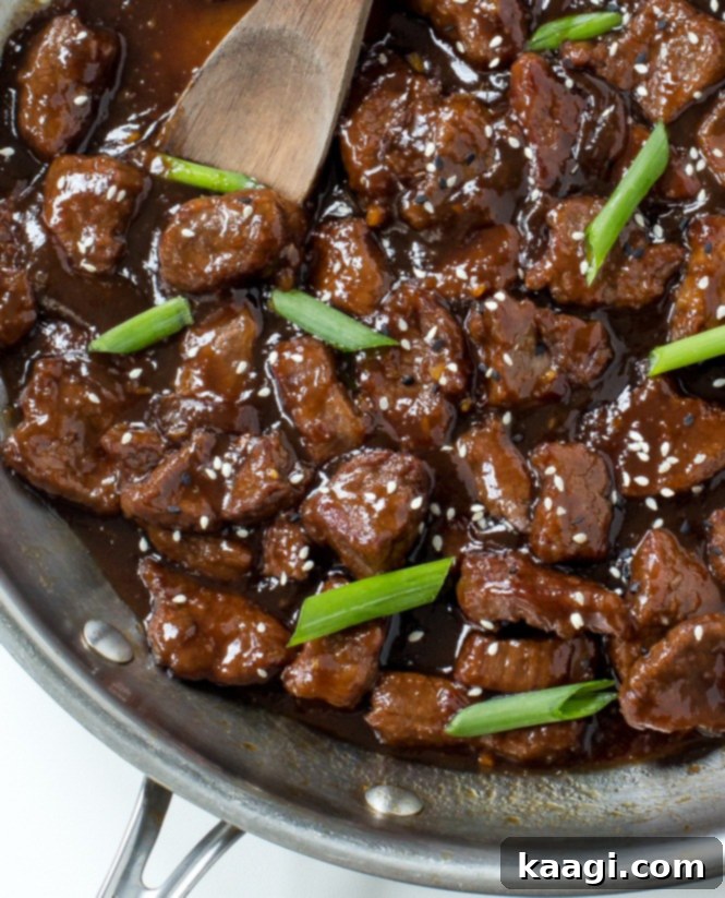A skillet filled with succulent Chinese Mongolian Beef, garnished with fresh green onions and sesame seeds.