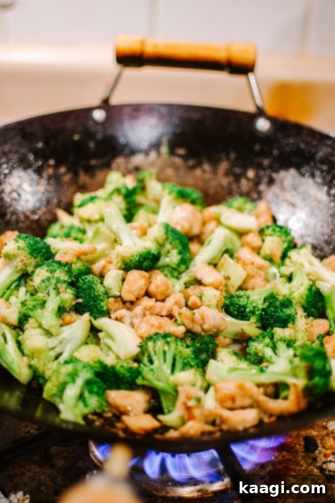 A large wok filled with sizzling chicken and broccoli stir-fry, a quick and healthy meal.