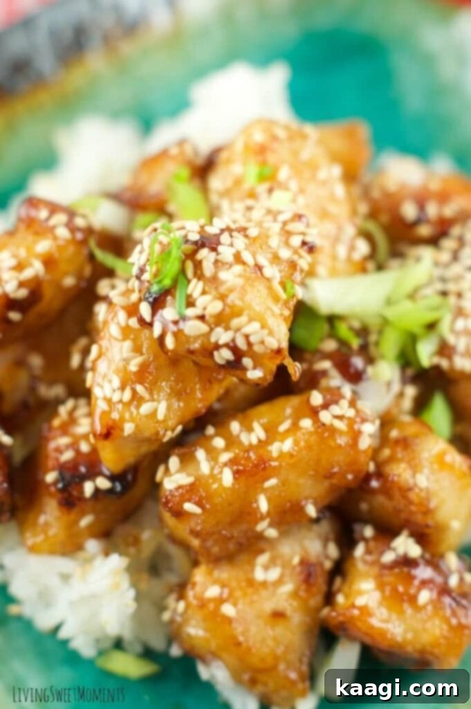 A close-up of glistening baked honey sesame chicken, generously sprinkled with sesame seeds.