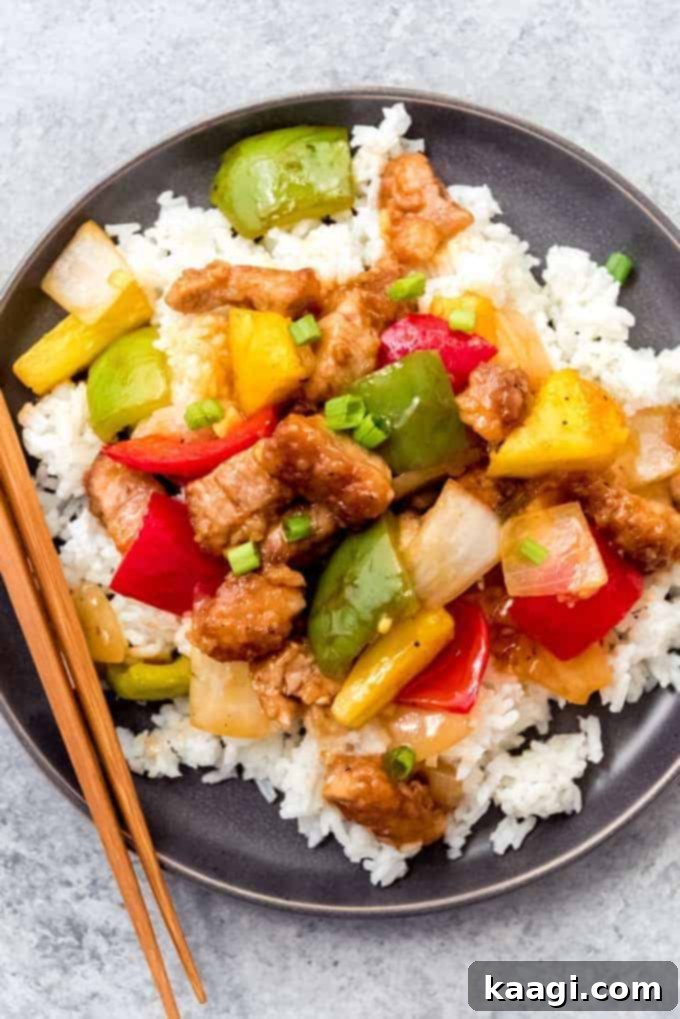 An overhead close-up of vibrant Sweet and Sour Pork with fresh pineapple and chopsticks on the side.