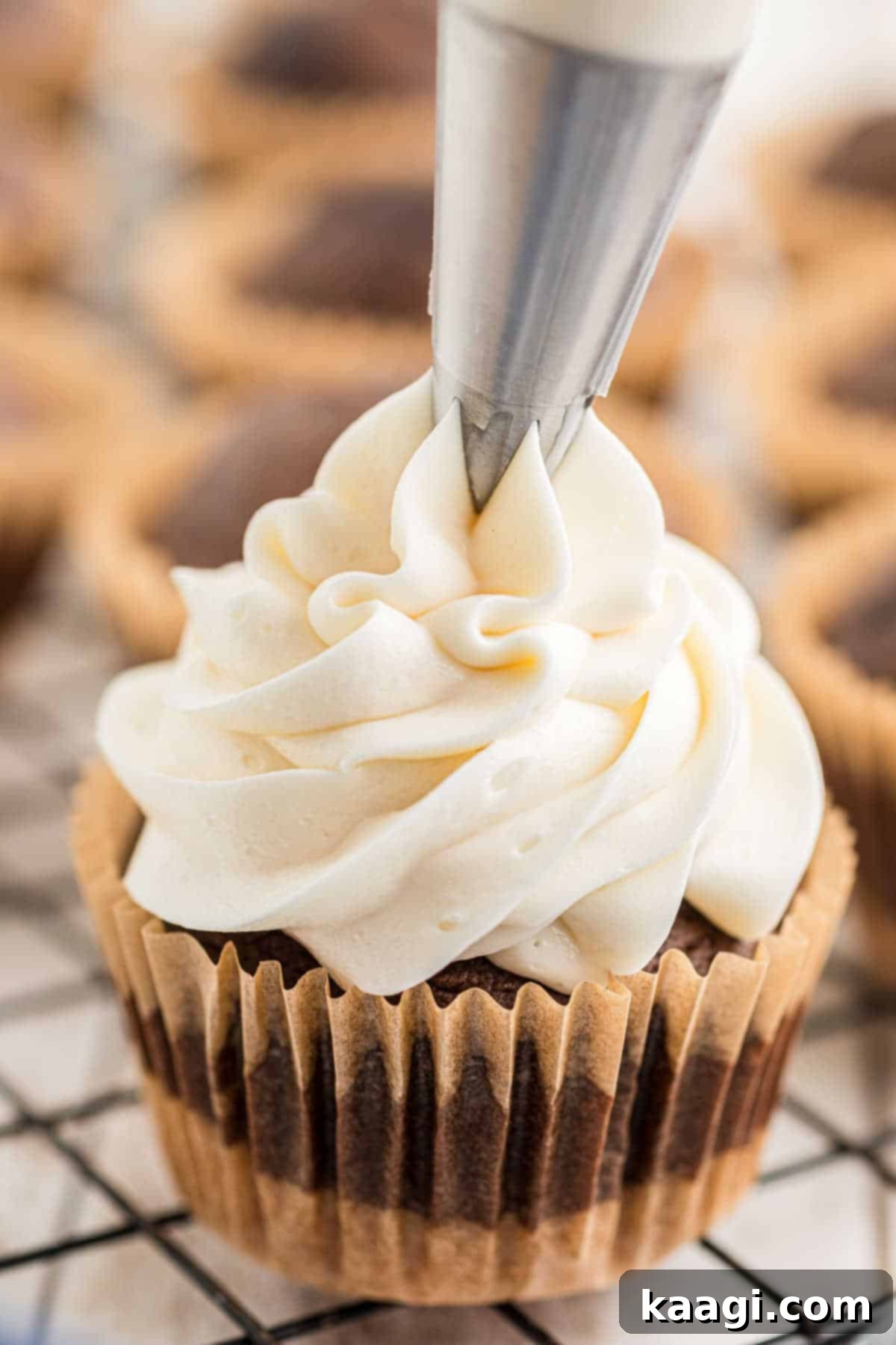 Close up of fluffy marshmallow frosting being expertly piped onto a S'mores cupcake, ready for final decorations.