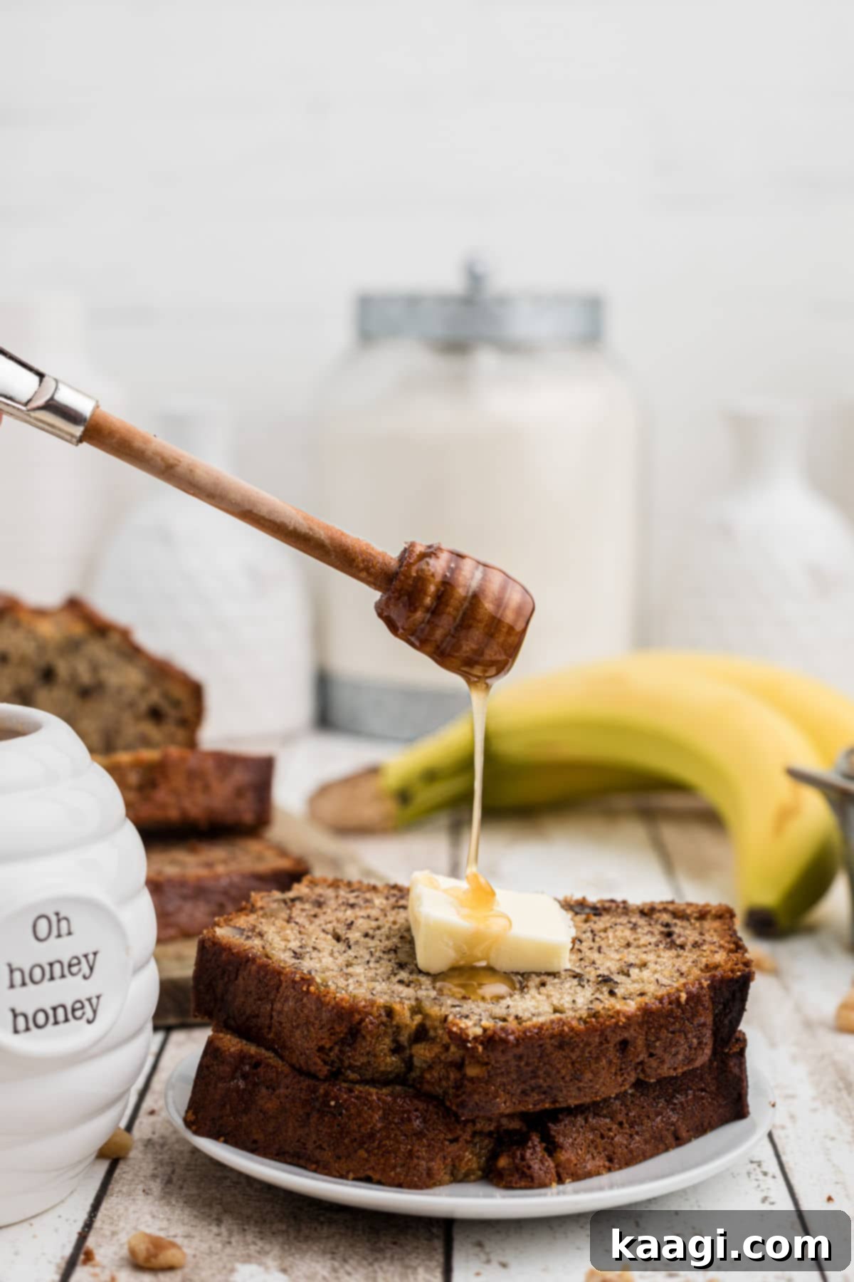 Mayo Magic Banana Bread 6 2 slices of banana bread with a butter slice on top with honey being drizzled on top - bananas in the background