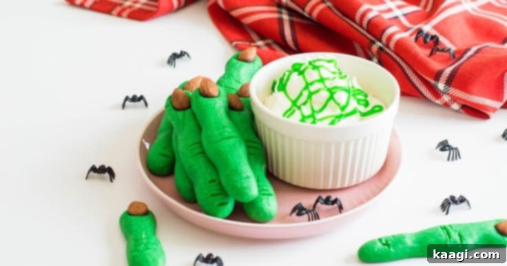 Spooky Witch Finger Cookies with green frosting and almond 'fingernails' on a rustic cutting board.
