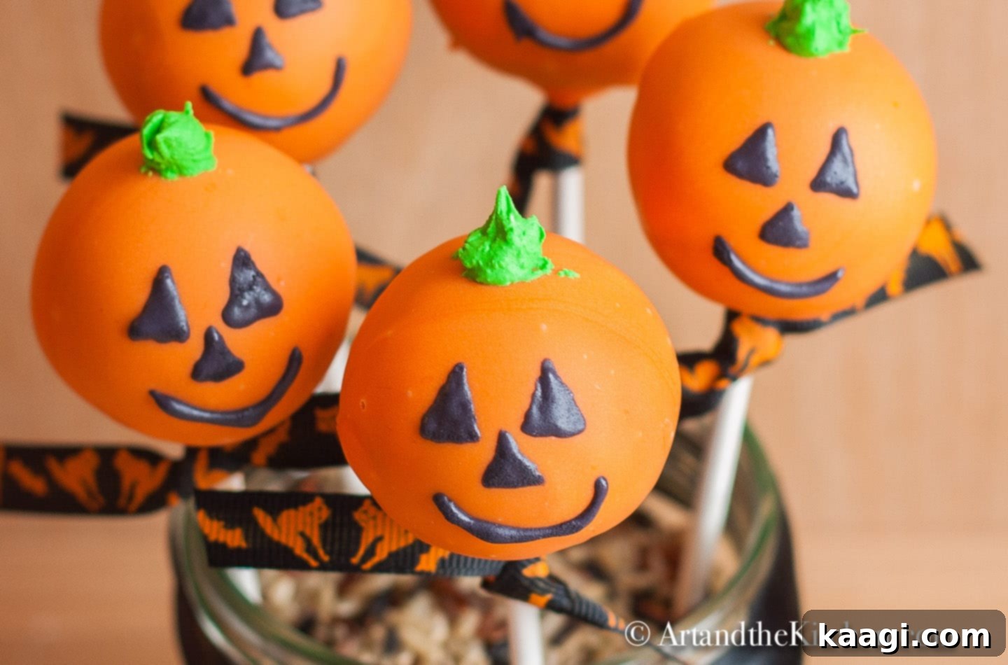 Adorably decorated Halloween Cake Pops shaped like Jack-O-Lanterns, displayed on a cake pop stand.