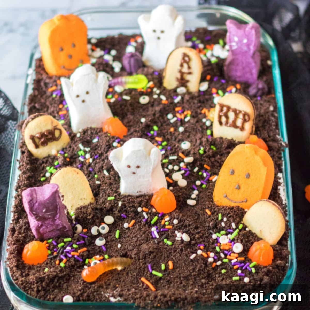 A spooky Halloween graveyard poke cake, decorated with crushed cookies for dirt, candy tombstones, and ghostly figures.