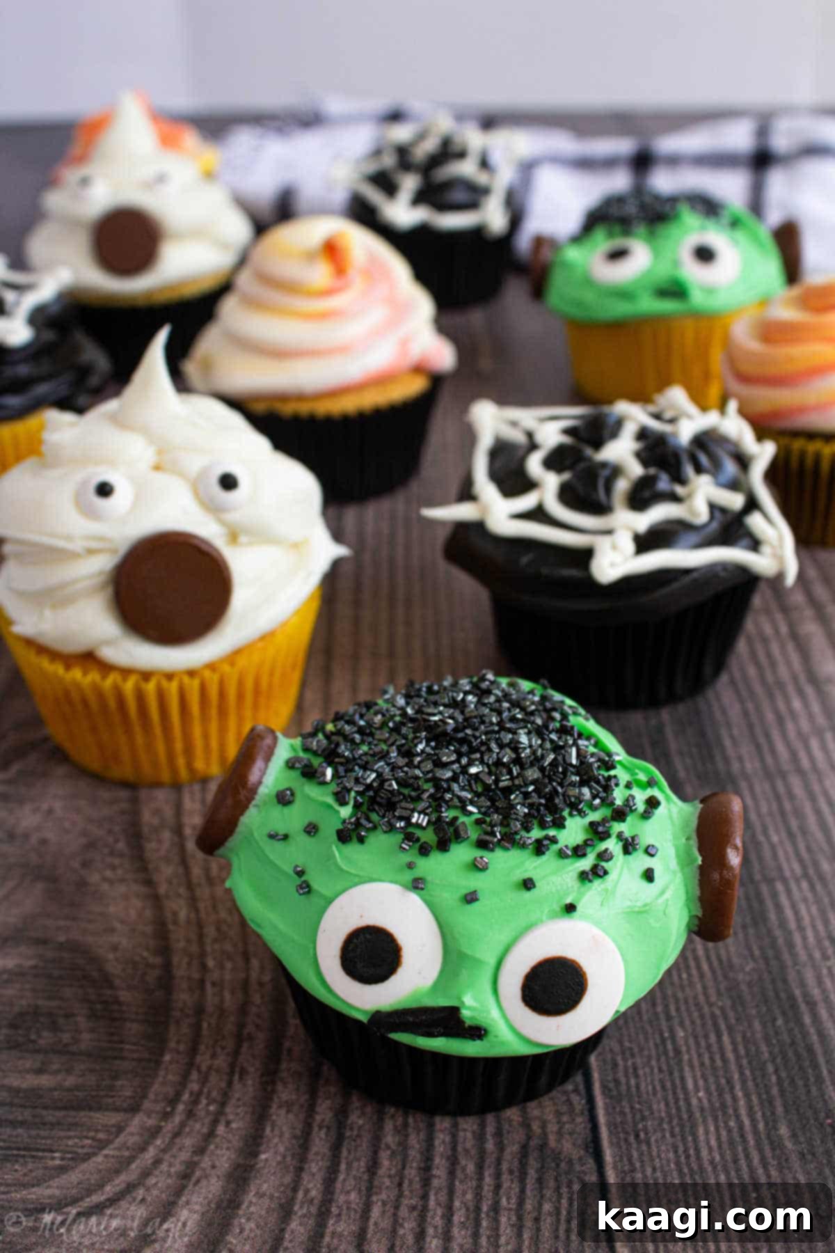 Franken-Fabulous Cupcakes 5 A close-up display of various Halloween cupcakes including ghost cupcakes, Frankenstein cupcakes, and spiderweb cupcakes.