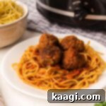 A close-up of a perfectly plated spaghetti and meatballs, with a simmering crock pot subtly blurred in the background.
