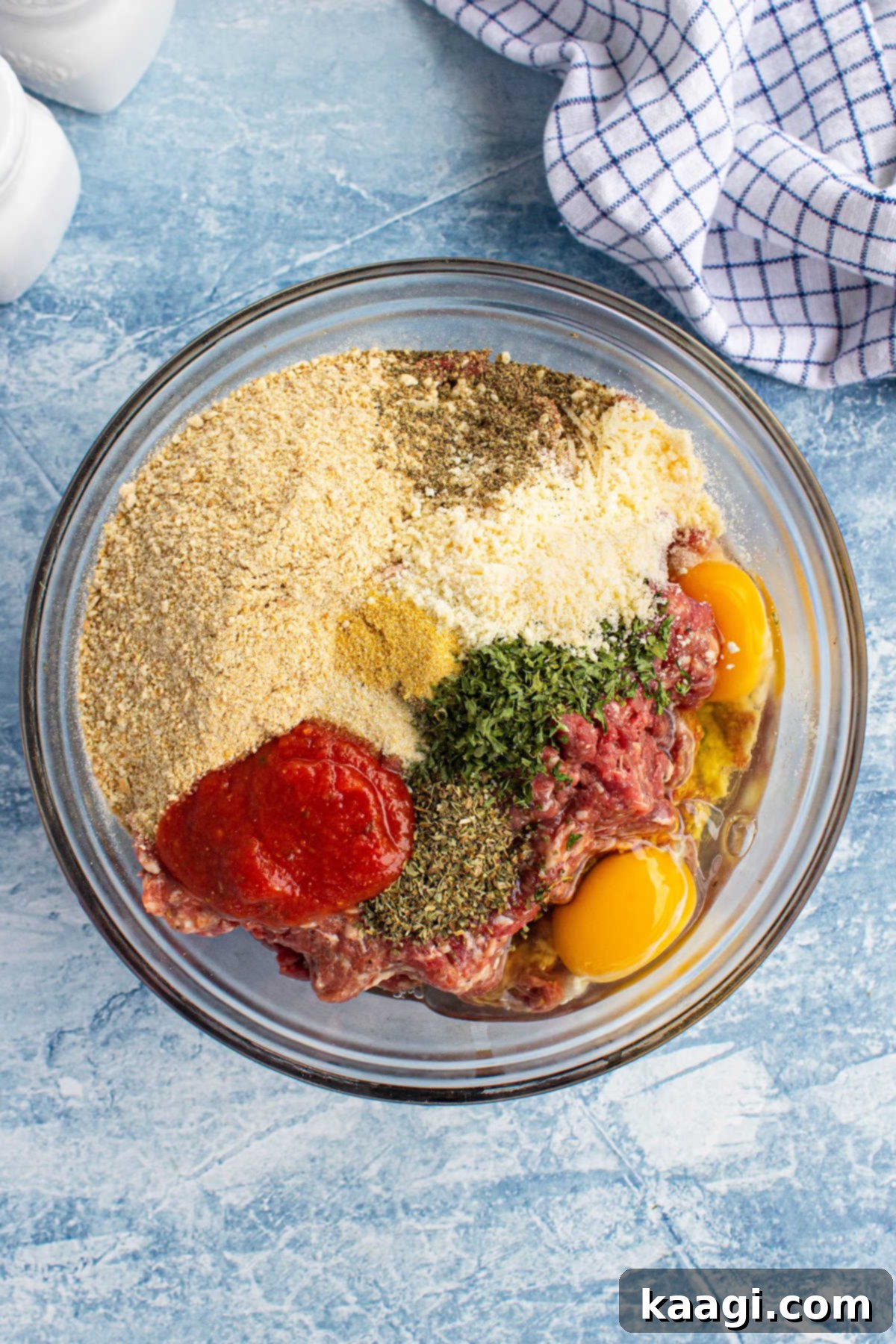 A large mixing bowl containing ground beef, Italian sausage, breadcrumbs, eggs, and seasonings, ready to be mixed for meatballs.