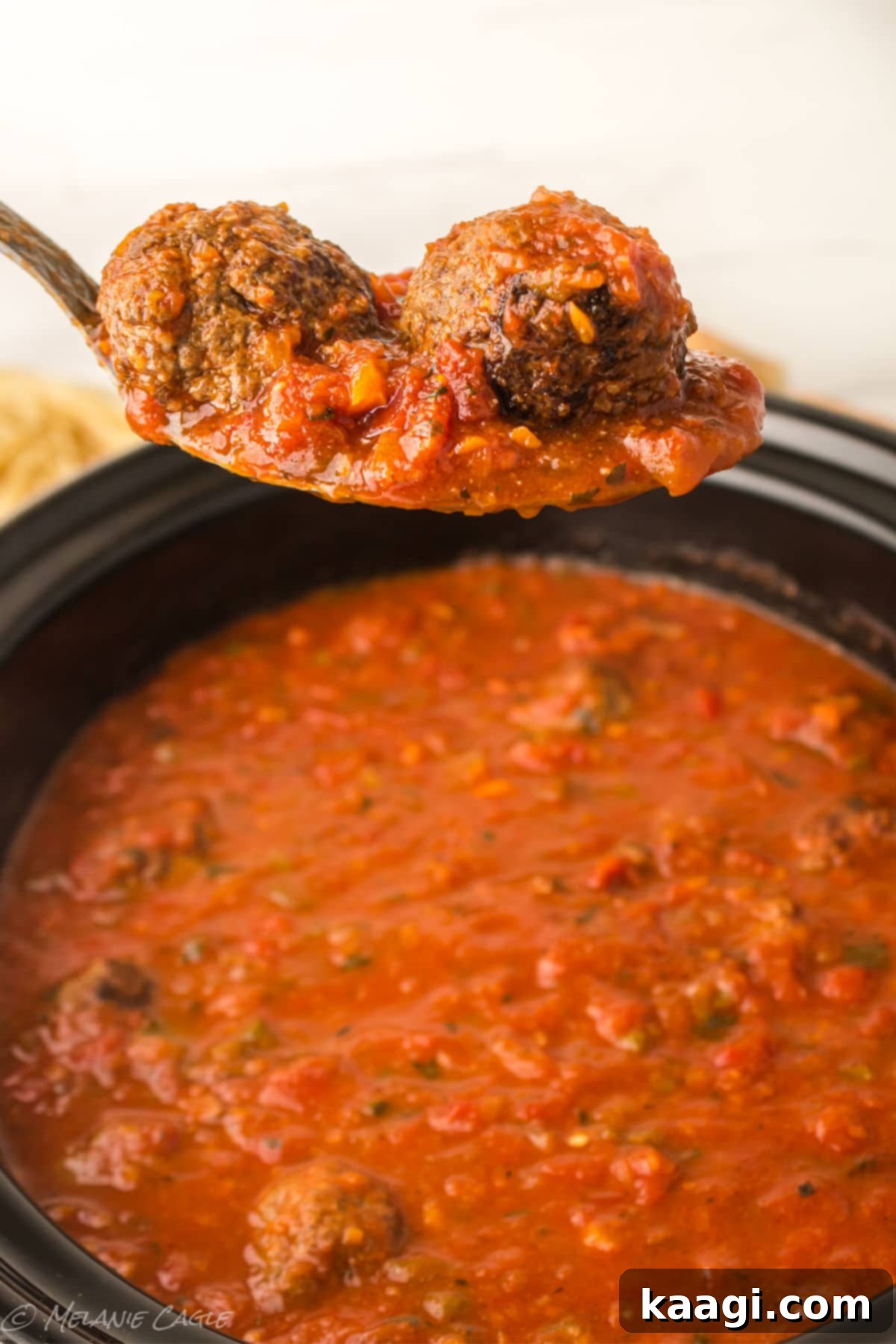 A serving spoon lifting a generous portion of spaghetti and meatballs from a large pot, ready to be dished out.
