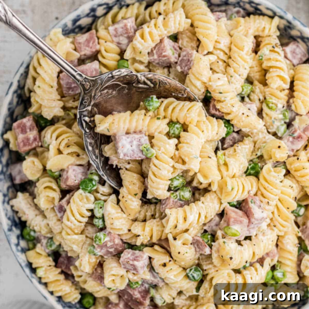 Close up of a bowl of creamy Ruby Tuesday ham and pea pasta salad with a spoon.