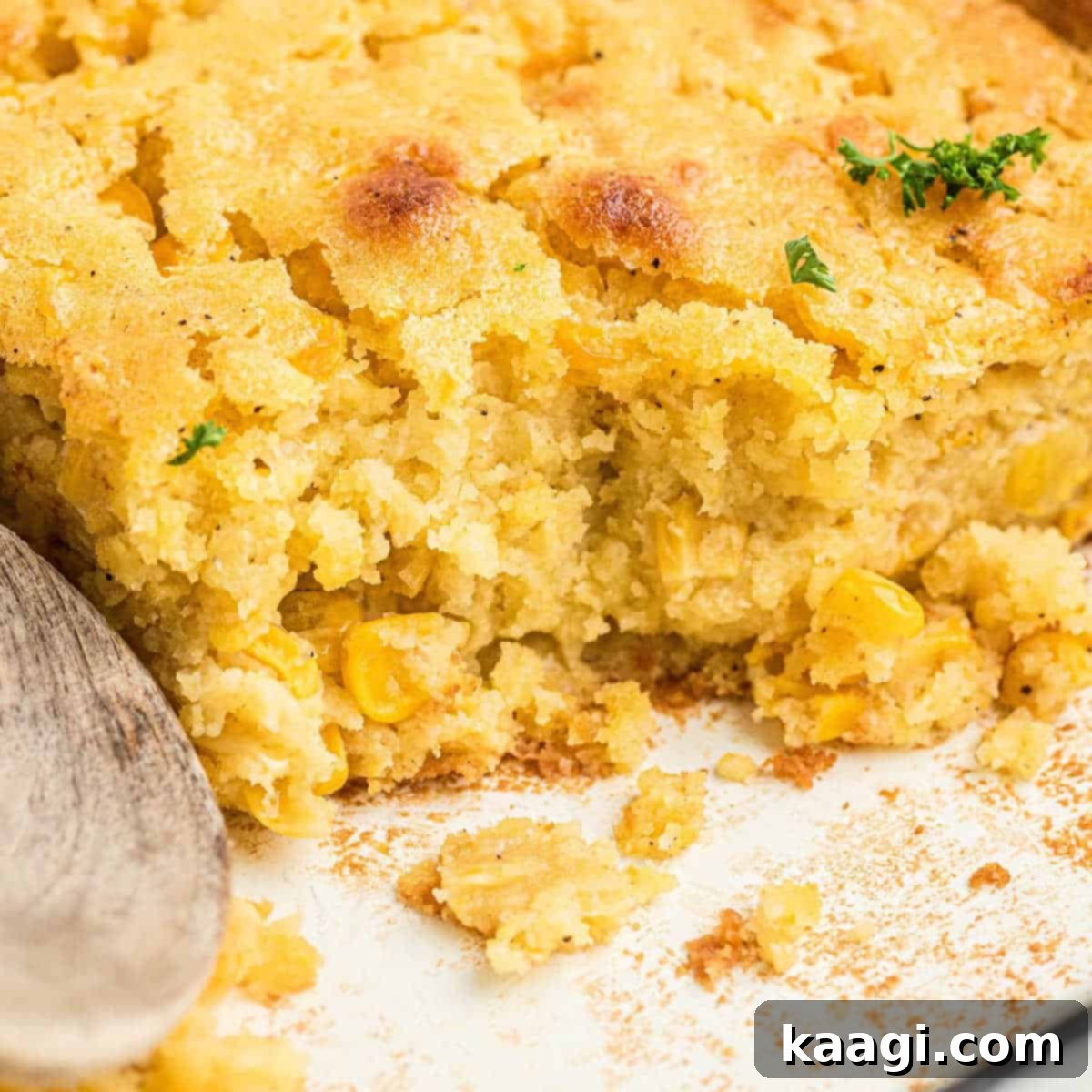 Close up shot of a warm, inviting dish of cornbread pudding with a wooden spoon resting.