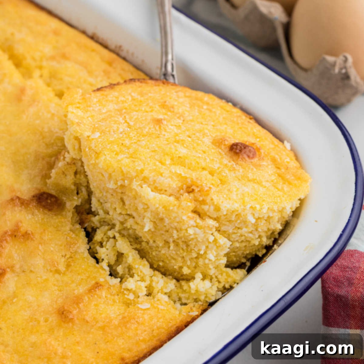 A golden piece of southern spoon bread being lifted out of the pan, showing its soft texture.