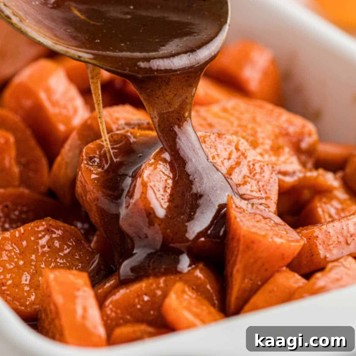 A dish full of glistening candied yams with a rich treacle being poured over the top.
