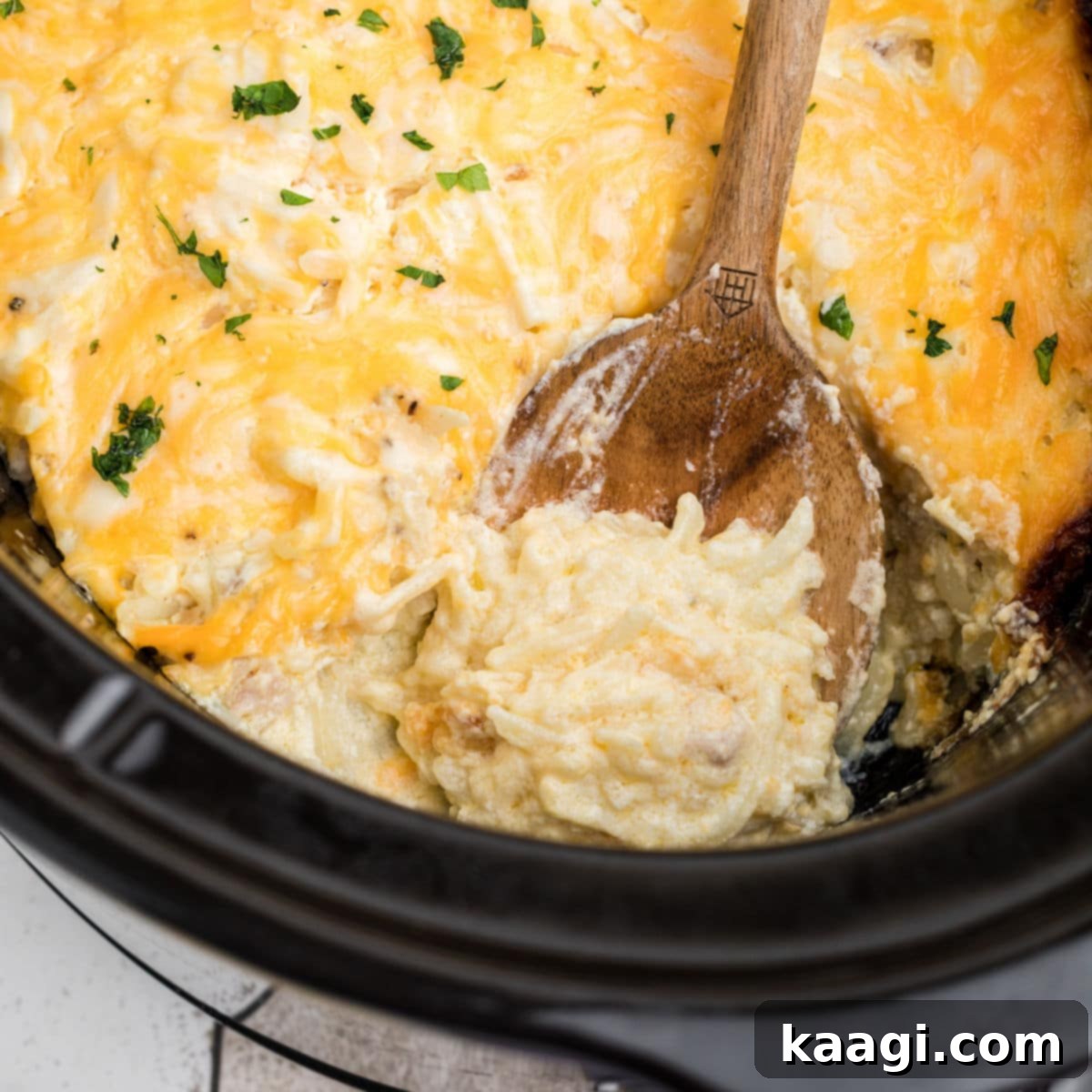 A close-up of a spoon digging into a bubbly, cheesy hash brown casserole from Cracker Barrel, made in a crockpot.