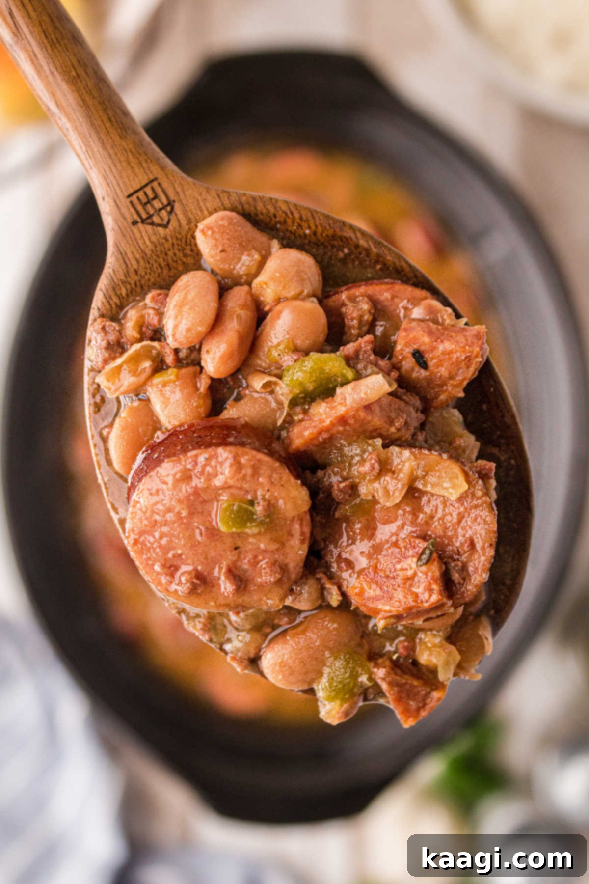 Close up of creamy pinto beans and sausage on a spoon over a slow cooker, showcasing the rich texture and delicious ingredients.